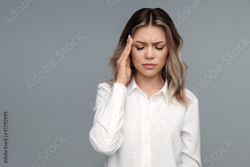 Frustrated young businesswoman suffering from headache or migraine tough hurting temple to relief pain. Tired business lady or office worker in white shirt feeling bad from stress at work or overwork