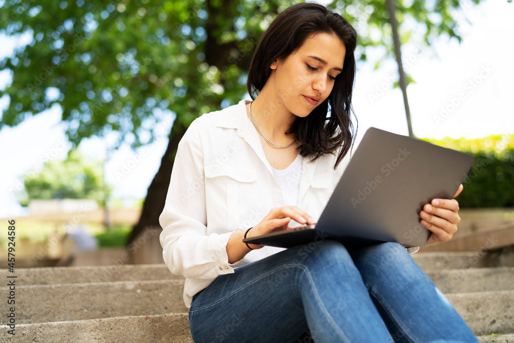 Young businesswoman sitting on steps outdoors and working on laptop. Beautiful girl learning in the park. Young businesswoman sitting on steps outdoors and working on laptop. Beautiful girl learning in the park.