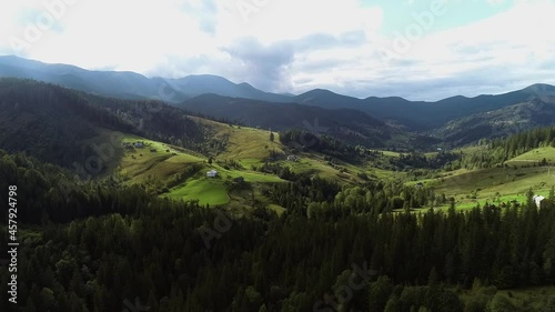 Flying over autumn mountain village with forests, hills and countryside meadows. Sun rays emerging though the clouds in the mountains. Aerial view of picturesque landscape of Carpathian Mountains. 4k