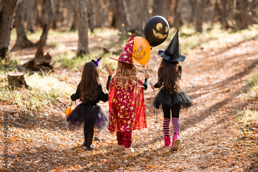 three little girls in witch costumes laugh, conjure, walk through the autumn forest with baskets for sweets in the shape of pumpkins. halloween concept, lifestyle . High quality photo three little girls in witch costumes laugh, conjure, walk through the autumn forest with baskets for sweets in the shape of pumpkins. halloween concept, lifestyle . High quality photo