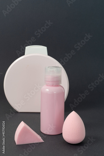Face care set: beauty blenders and face serum in pink colour on a dark grey background 