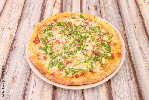 Iberian ham pizza with arugula, mozzarella cheese and grated cheese with tomato on wooden table