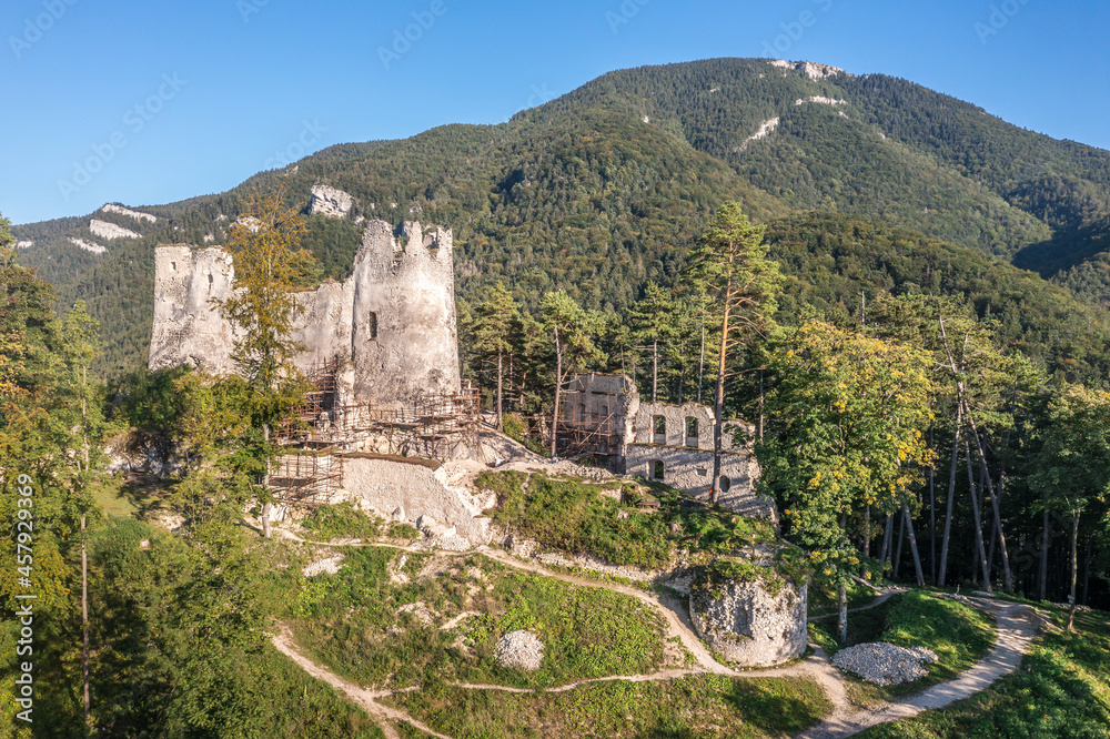 Aerial view of medieval Blatnica Gothic hilltop castle ruin above the village in a lush green forest area with towers and restoration work in Slovakia