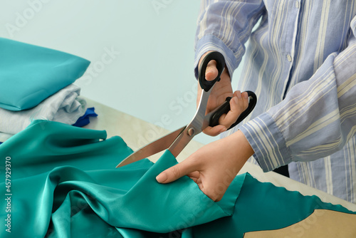 Young woman cutting fabric at table