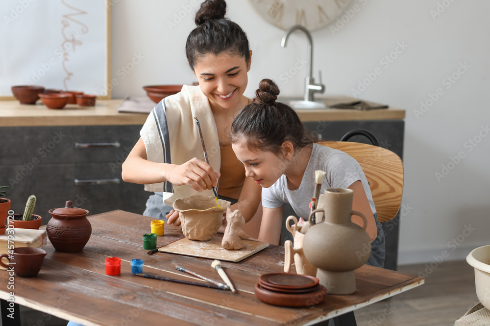 Fototapeta premium Little girl with her mother painting ceramic pot at home