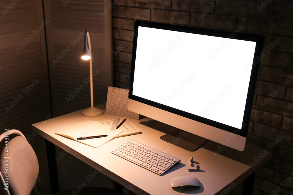 Stylish workplace with modern computer and lamp in evening Stylish workplace with modern computer and lamp in evening