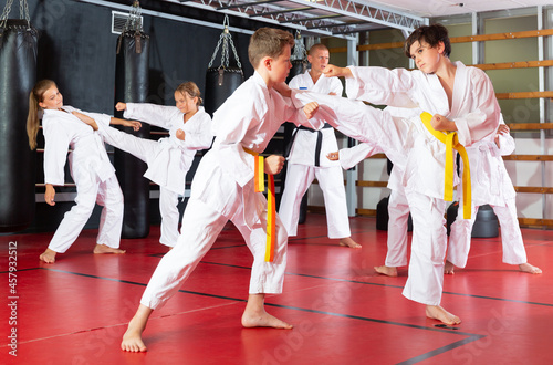 Group of preteen children practicing taekwondo kicks in pairs at sport gym