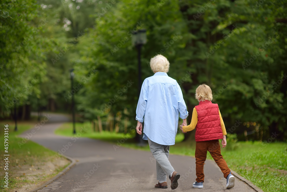 Elderly grandmother and her little grandchild walking together in sunny summer park. Grandma and grandson. Two generations of family. Elderly grandmother and her little grandchild walking together in sunny summer park. Grandma and grandson. Two generations of family.
