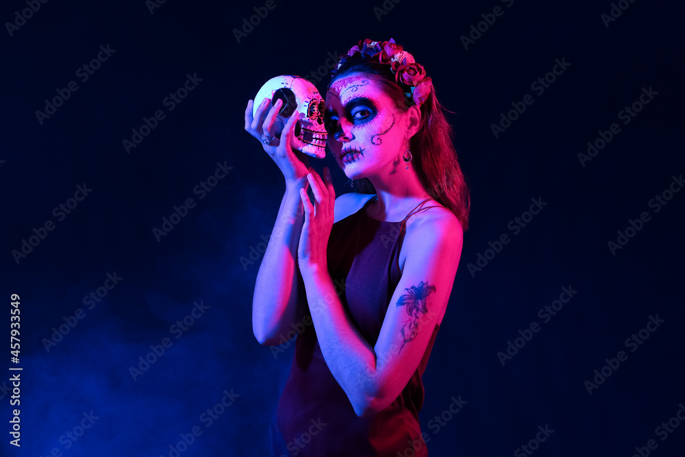 Young woman with painted face and sugar skull for Mexico's Day of the Dead (El Dia de Muertos) on dark background Young woman with painted face and sugar skull for Mexico's Day of the Dead (El Dia de Muertos) on dark background