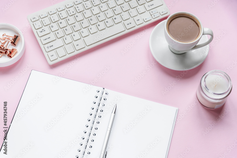 Cozy workplace with blank notepad, keyboard, cup of coffee and candle. Top view, flat lay. Pink background Cozy workplace with blank notepad, keyboard, cup of coffee and candle. Top view, flat lay. Pink background