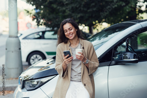 Young pretty woman with cup of coffee and texting blog on tablet in autumn park near vehicle