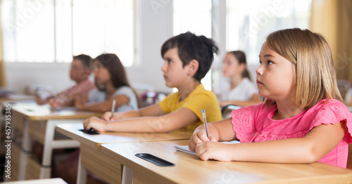 Young girls and boys sitting at desks in classroom during lesson.