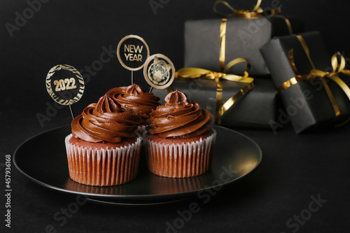 Tasty cupcakes for New Year 2022 celebration on dark background