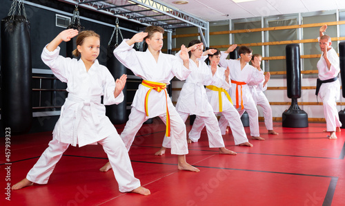 Karate kids in kimono performing kata moves with their teacher in gym during group training.