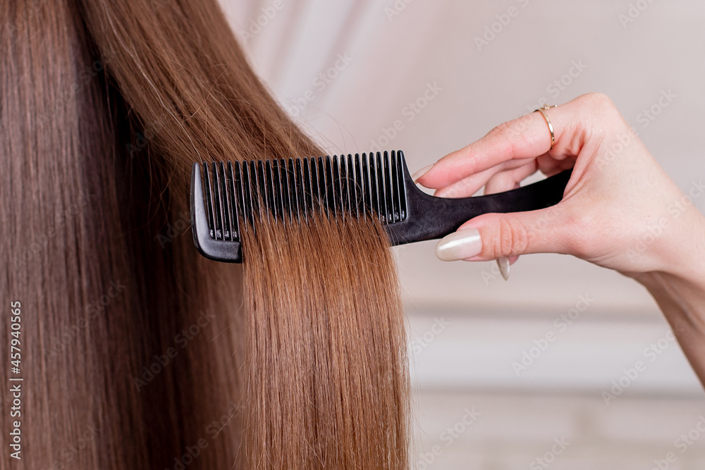 Fototapeta premium Hairdresser's hand brushing long brunette hair in beauty salon