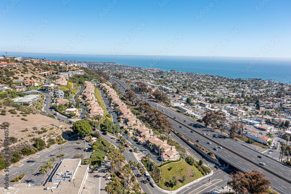 Birds eye view of apartments on a hillside, homes, ocean, and freeway visible 