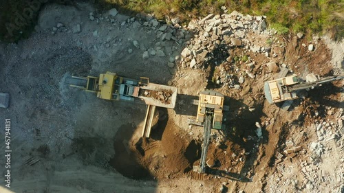 Drone shot of two Excavators loading into a transportable industrial stone crusher with granite for gravel production at a construction site. Heavy excavators throw large rocks with buckets and smash  photo