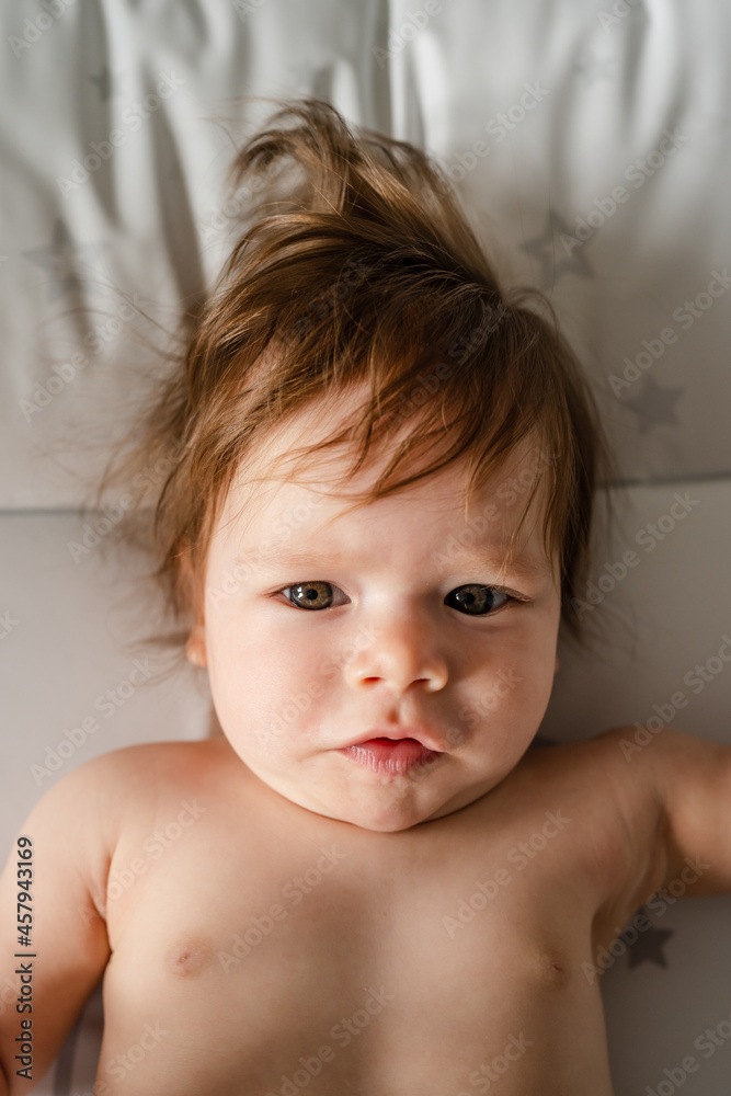 Close up on small caucasian baby naked lying on the bed top view serious child looking to the camera Close up on small caucasian baby naked lying on the bed top view serious child looking to the camera