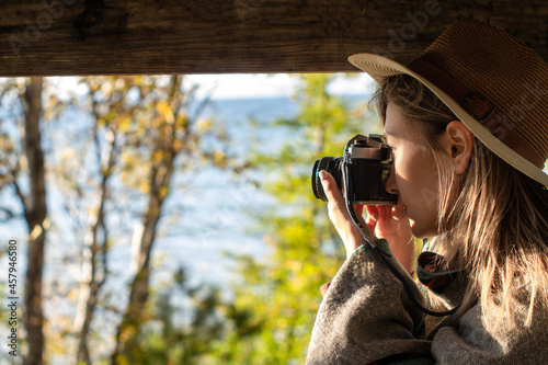 side view of a woman in hat in the park by the sea taking photo on a film camera