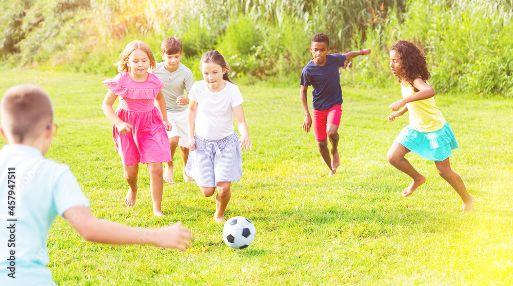 Boys and girls playing football on green grass together outdoors.