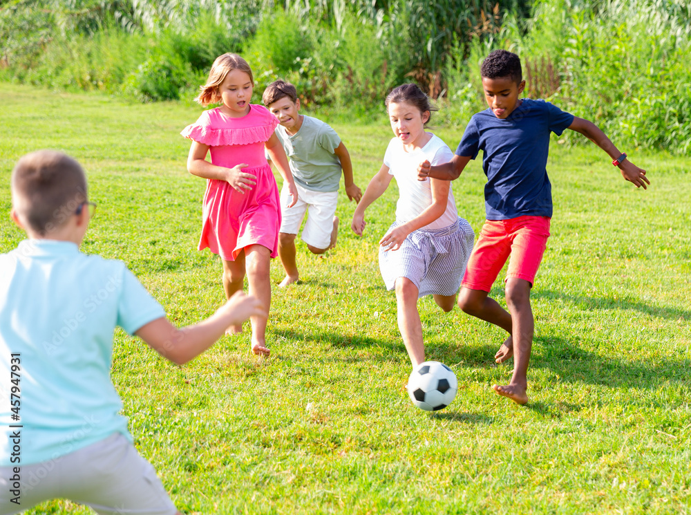 Obraz premium Group of barefoot kids playing football on grass. They're kicking ball and having fun.