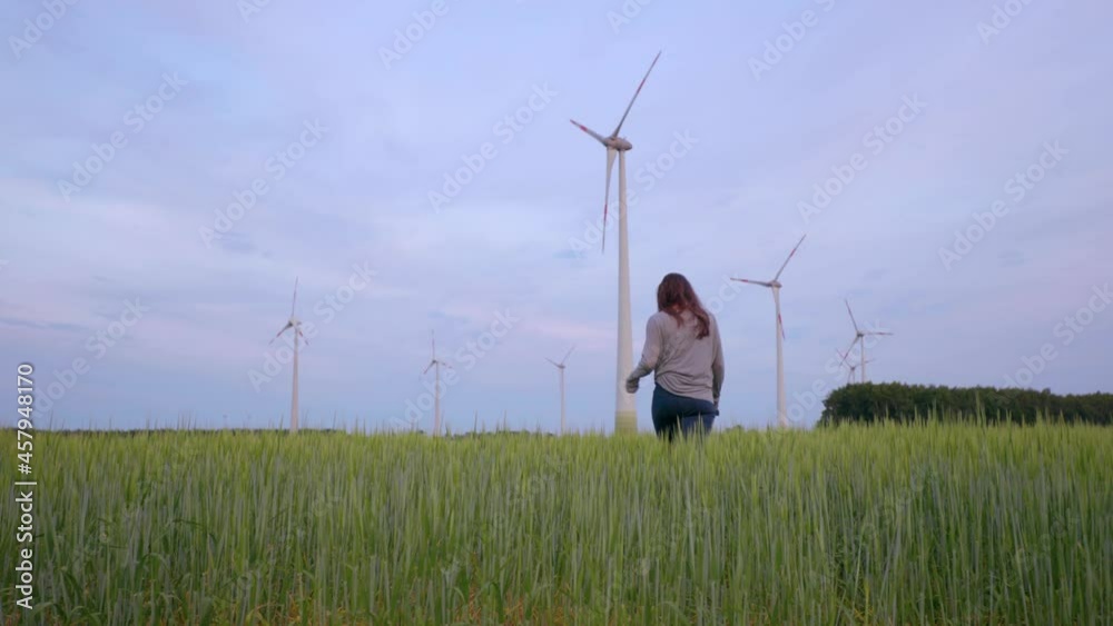 custom made wallpaper toronto digitalYoung female is walking through grain field with high grass towards big windmills for renewable energy technology park with tall turbines in dutch farmland low shot 4k