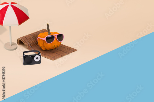 Creative autumn idea with sun umrela and pumpkin hipster in sunglasses laying on the beach.