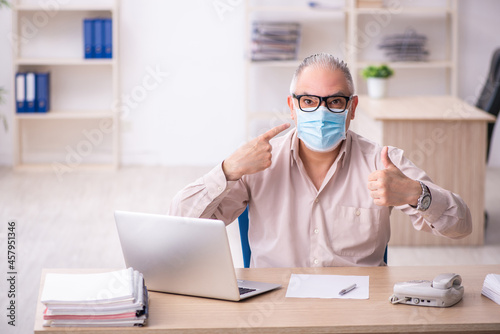 Old male employee working at workplace during pandemic
