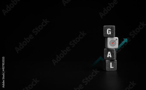Goals concept. Goal, word and target icon sign on black and white stacking cube blocks with arrow up, growth graph chart on dark background with copy space.