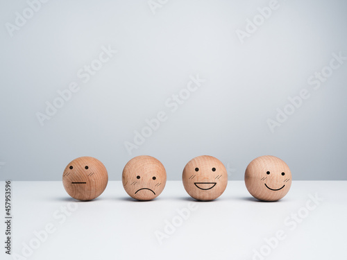 Customer service evaluation, feedback, and satisfaction survey concept. Wooden balls with a cute happy smiling emoticon with another emotional faces on white background with copy space.
