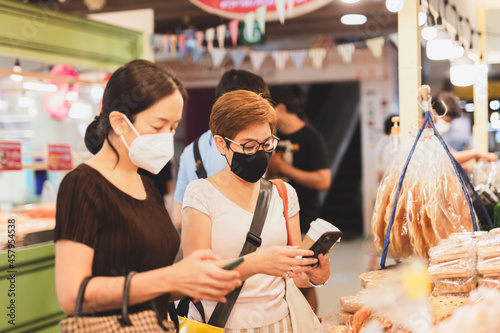Female customer in protective mask make contactless mobile payment in retail shop.