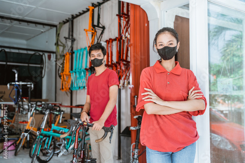 saleswoman in mask looking at camera with folded hands and a man holding a bicycle