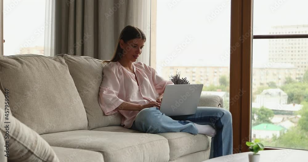Confident young lady freelancer engaged in remote work from home sitting on sofa using laptop. Millennial female student study online prepare digital homework think on answer electronic test questions Confident young lady freelancer engaged in remote work from home sitting on sofa using laptop. Millennial female student study online prepare digital homework think on answer electronic test questions
