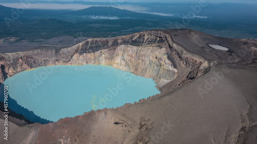 Turquoise acidic lifeless lake in the crater of a volcano. Deposits of sulfur on the surface. On the steep rocky slopes, devoid of vegetation, the shadow of a helicopter. Aerial view. Kamchatka