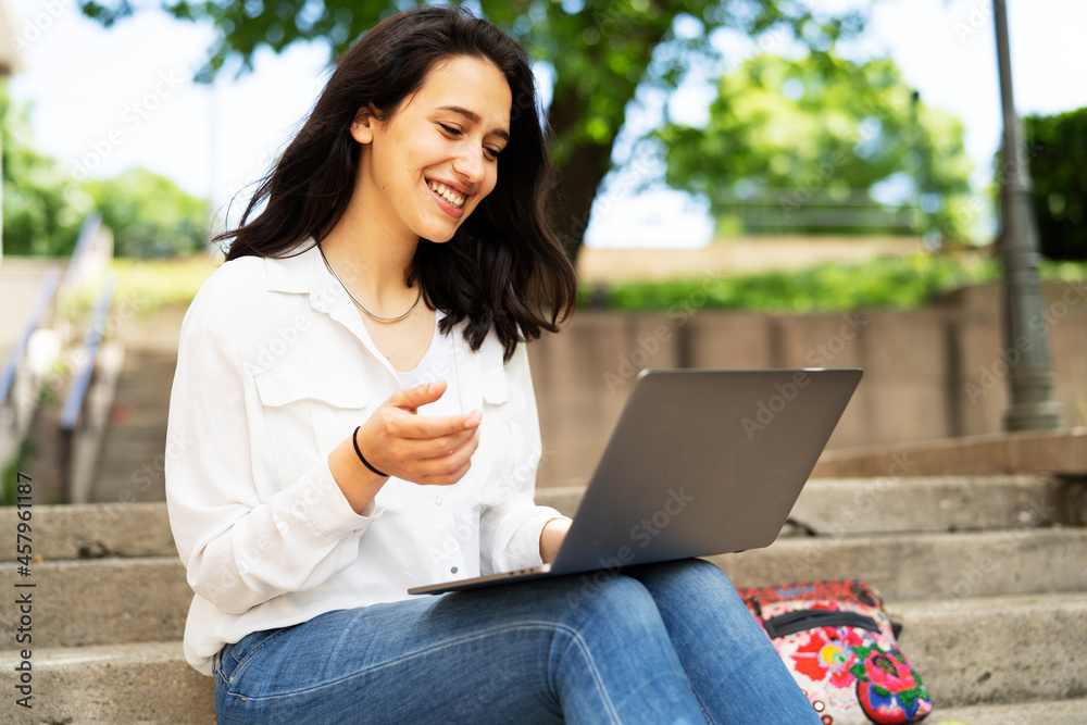 Young businesswoman sitting on steps outdoors and working on laptop. Beautiful girl learning in the park.