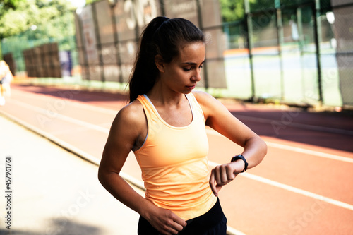 Young beautiful woman training outdoors. Female runner using smart watch..
