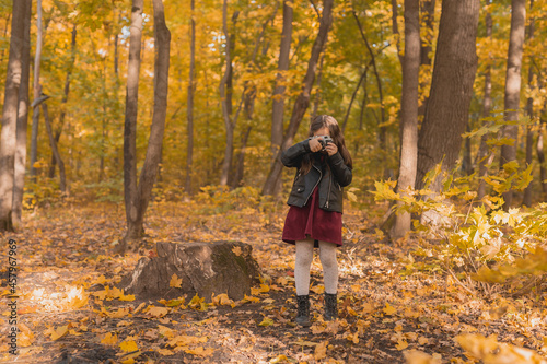 A little girl take a photo with old retro camera in autumn nature. Leisure and hobby concept. © satura_