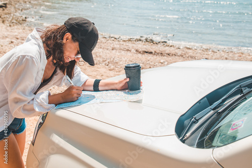 woman checking map on car hood drinking coffee at summer sea beach © phpetrunina14