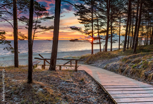 Fototapeta Naklejka Na Ścianę i Meble -  Coastal landscape at dawn. Wooden footpath among pine forest leading to sandy beach of the Baltic Sea