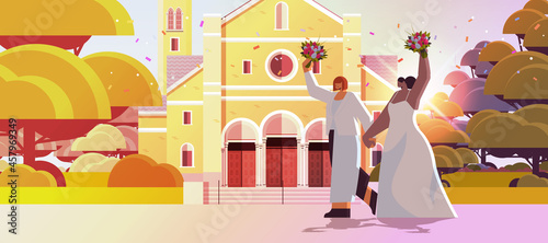 newlywed lesbian couple with flowers standing together near church transgender love LGBT community wedding celebration