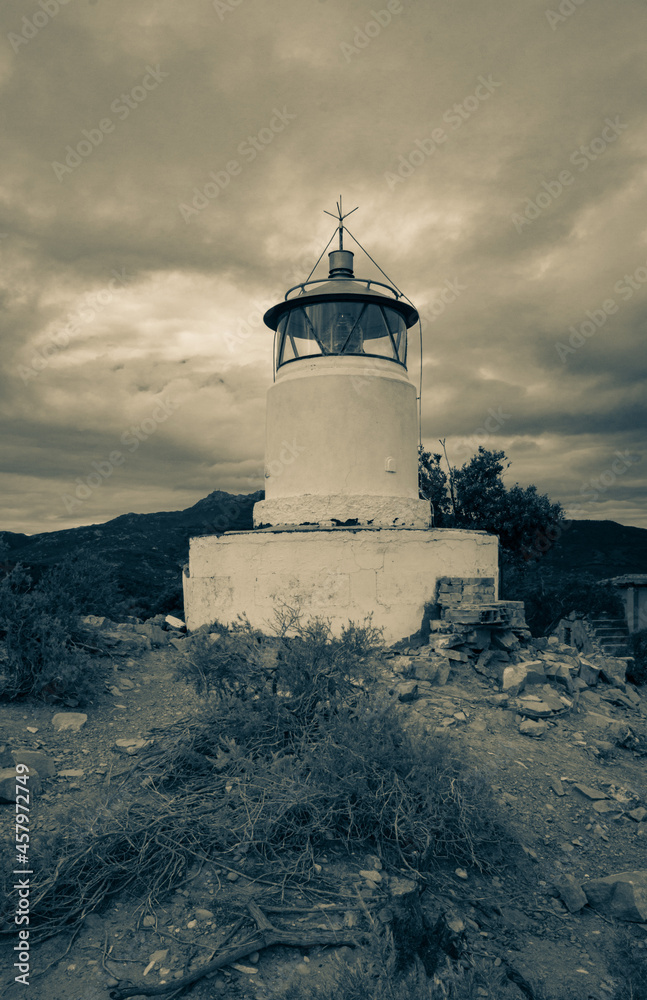 View on the old white lighthouse of Monte Poro under dramatic sky, Elba island, Italy. Old abandoned lighthouse in the middle of the bushes. Vertical image, split tones.