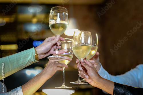 Toast at the restaurant. Detail on the clinkering white wine glasses. Concept of friends having a toast together by raising their wineglasses.