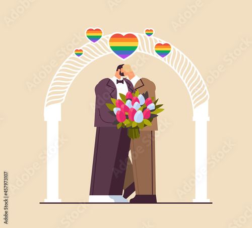 newlywed gay couple with flowers kissing near wedding arch transgender love LGBT community wedding celebration