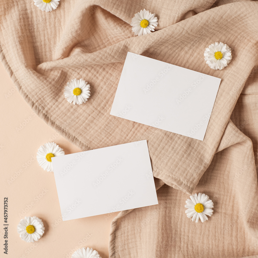Flatlay of aesthetic Parisian styled business branding template. Blank paper sheet card with mockup copy space, chamomile flower buds and muslin cloth on neutral beige background. Flat lay, top view