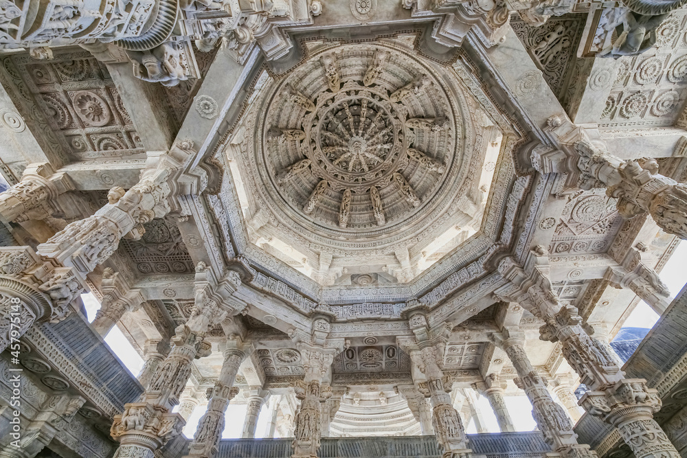 Historic Dilwara temple interior architecture with view of intricately carved stone ceiling with columns with beautiful artwork