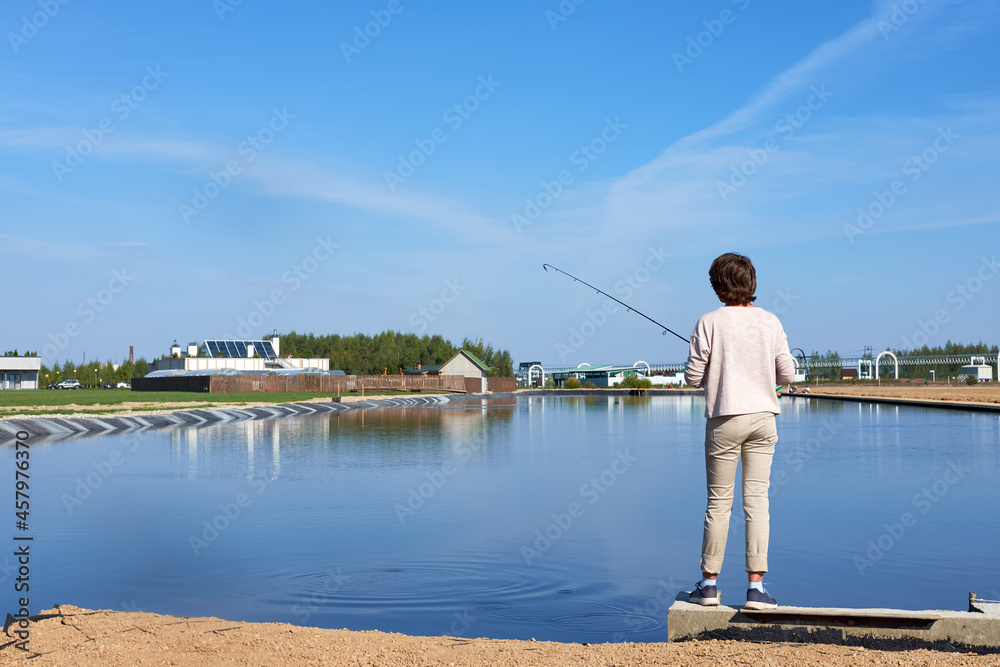 angler woman in light clothes is catching spinning fish in pond on the summer sunny day angler woman in light clothes is catching spinning fish in pond on the summer sunny day
