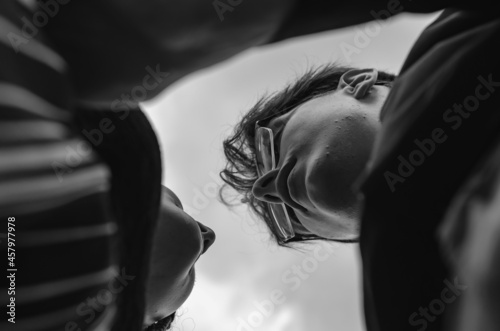 An unusual portrait of a heterosexual couple in love against the sky. A young man and a young woman preparing for a tender kiss. Bottom-up view. Selective focus. Black and white photo.