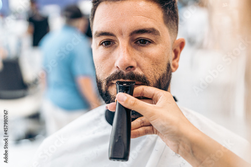 Hand grooming the moustache of a man with an electric razor in a barber shop