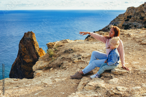 Daughter sitting with mom on the shore looking at seascape 