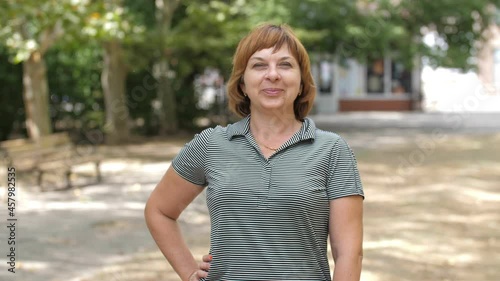Gleeful blonde woman standing and smiling happily in a sunny park in summer 